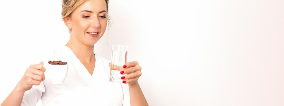 Coffee with water. The female nutritionist holds a cup of coffee beans and a glass of water in her hands on white background