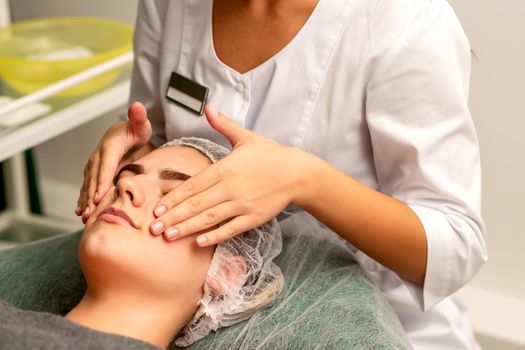 Face massage. Beautiful caucasian young white woman having a facial massage with closed eyes in a spa salon