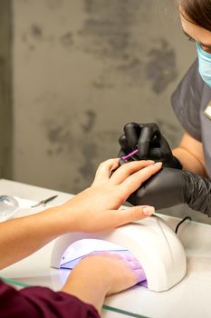 Professional manicure. A manicurist is painting the female nails of a client with purple nail polish in a beauty salon, close up. Beauty industry concept