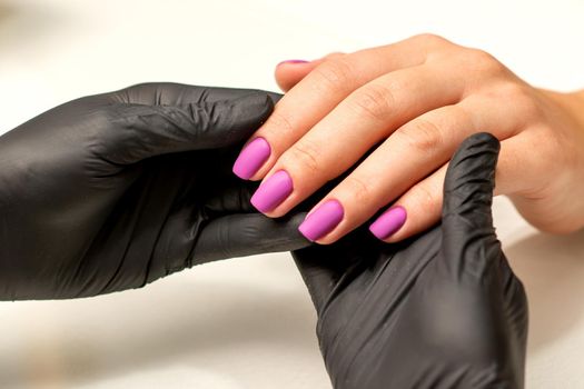 A manicurist holds beautiful young female hands showing finished purple, pink polish manicure in a nail salon