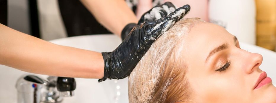 Young caucasian woman with closed eyes getting washing hair by a professional hairdresser in a beauty hair salon