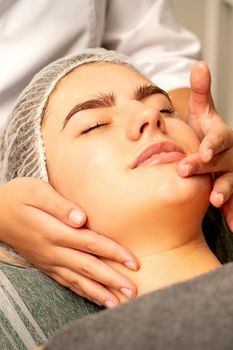 Face massage. Beautiful caucasian young white woman having a facial massage with closed eyes in a spa salon