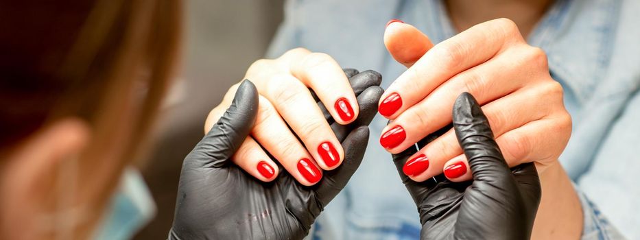 A manicurist holds beautiful young female hands showing finished red polish manicure in a nail salon