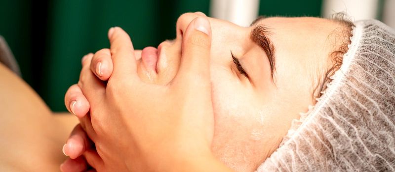 Face massage. Beautiful caucasian young white woman having a facial massage with closed eyes in a spa salon