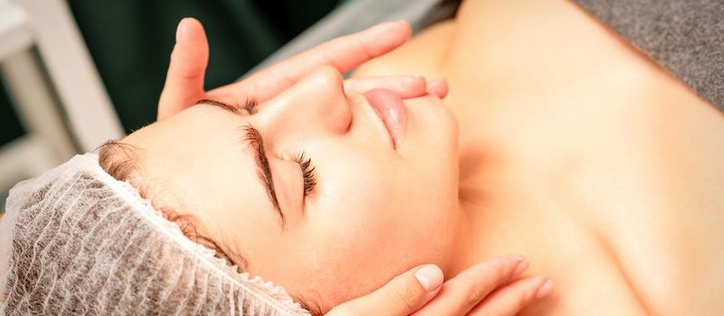 Face massage. Beautiful caucasian young white woman having a facial massage with closed eyes in a spa salon