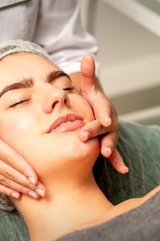 Face massage. Beautiful caucasian young white woman having a facial massage with closed eyes in a spa salon