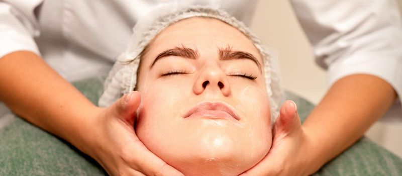 Face massage. Beautiful caucasian young white woman having a facial massage with closed eyes in a spa salon