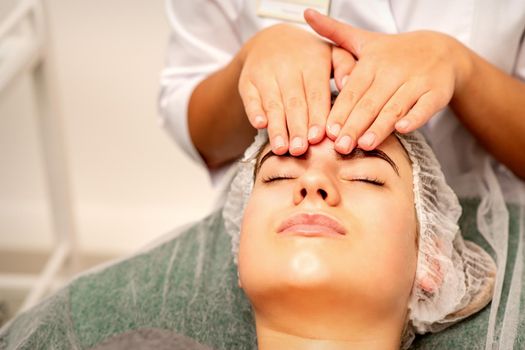 Head massage. Beautiful caucasian young white woman receiving a head and forehead massage with closed eyes in a spa salon
