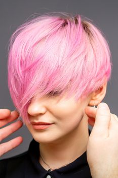 Hairdresser with hands is checking out and fixing the short pink hairstyle of the young white woman in a hair salon