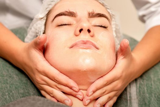 Face massage. Beautiful caucasian young white woman having a facial massage with closed eyes in a spa salon