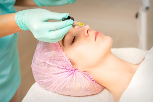 Young white woman getting acid organic retinol peel face skin with the pipette in a beauty clinic