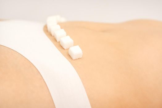 The concept of epilation, waxing, and intimate hygiene. Sugar cubes lying in a row on the bikini zone of a young white woman, close up