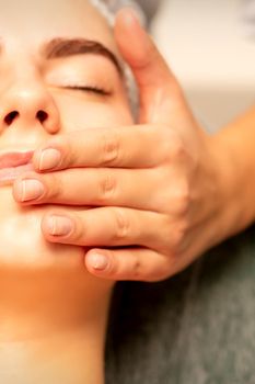 Beautiful young caucasian woman with closed eyes receiving a facial massage in a beauty salon