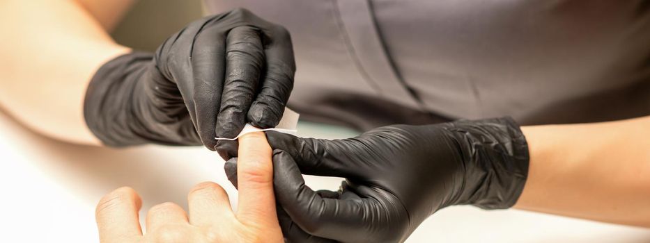 The manicurist finishes the procedure for red nail polishing and cleaning with a cotton napkin, pad, swab in a beauty salon, close up