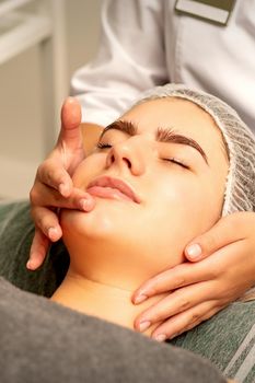 Face massage. Beautiful caucasian young white woman having a facial massage with closed eyes in a spa salon