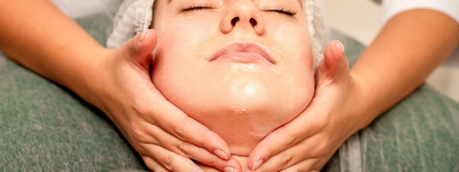 Face massage. Beautiful caucasian young white woman having a facial massage with closed eyes in a spa salon