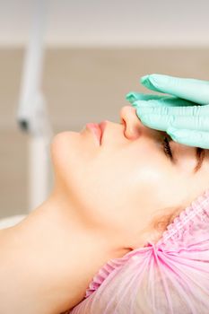 Cosmetologist with gloved hands applies a moisturizing mask with peeling cream on the female face. Facial cosmetology treatment. Procedures for facial care