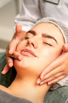 Face massage. Beautiful caucasian young white woman having a facial massage with closed eyes in a spa salon