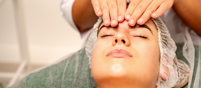 Head massage. Beautiful caucasian young white woman receiving a head and forehead massage with closed eyes in a spa salon