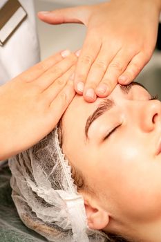 Head massage. Beautiful caucasian young white woman receiving a head and forehead massage with closed eyes in a spa salon