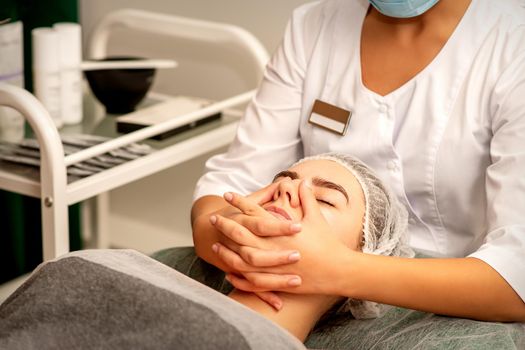 Beautiful young caucasian woman with closed eyes receiving a facial massage in a beauty salon
