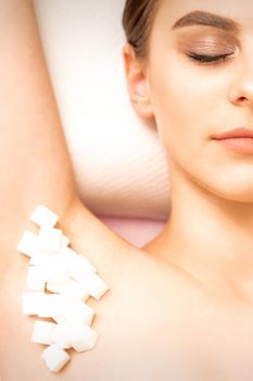 Sugaring, waxing concept. White sugar cubes lie down on the female armpit of the young white woman, close up