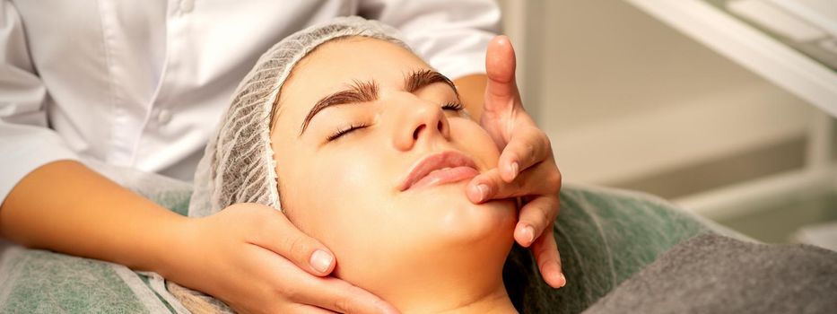 Face massage. Beautiful caucasian young white woman having a facial massage with closed eyes in a spa salon