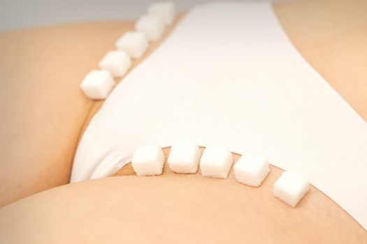 The concept of epilation, waxing, and intimate hygiene. Sugar cubes lying in a row on the bikini zone of a young white woman, close up