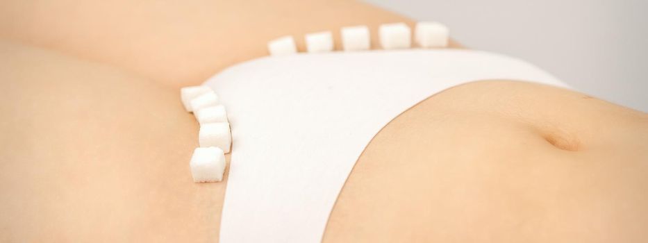 The concept of epilation, waxing, and intimate hygiene. Sugar cubes lying in a row on the bikini zone of a young white woman, close up