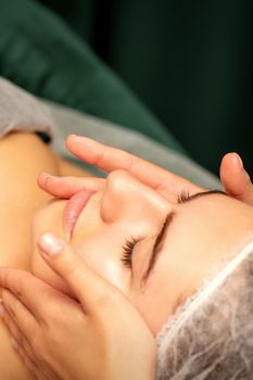 Beautiful young caucasian woman with closed eyes receiving a facial massage in a beauty salon