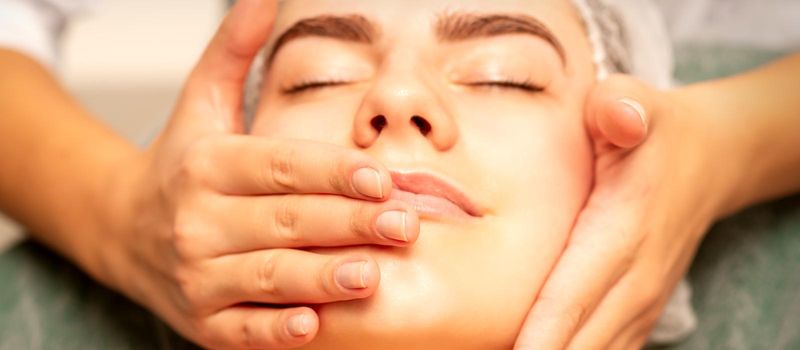 Beautiful young caucasian woman with closed eyes receiving a facial massage in a beauty salon