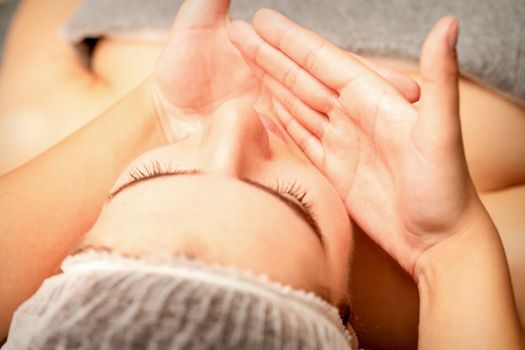 Beautiful caucasian young woman receiving a facial massage with closed eyes in spa salon, close up. Relaxing treatment concept