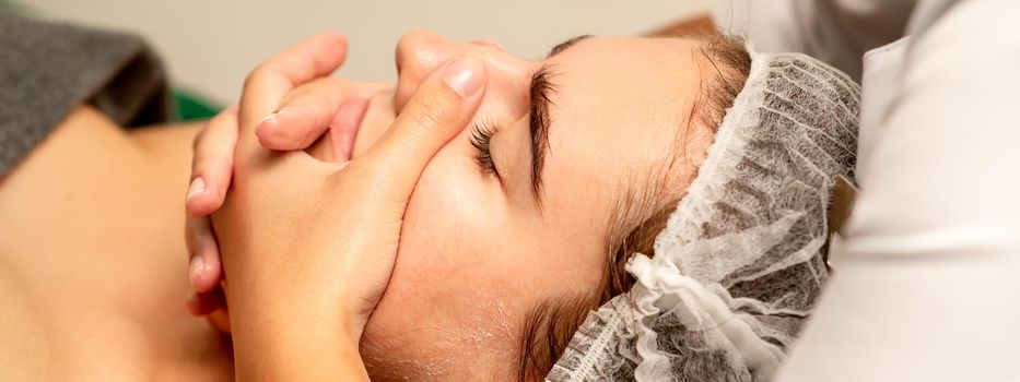 Face massage. Beautiful caucasian young white woman having a facial massage with closed eyes in a spa salon