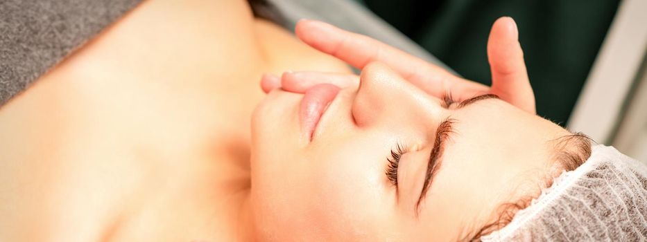 Face massage. Beautiful caucasian young white woman having a facial massage with closed eyes in a spa salon