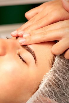 Head massage. Beautiful caucasian young white woman receiving a head and forehead massage with closed eyes in a spa salon