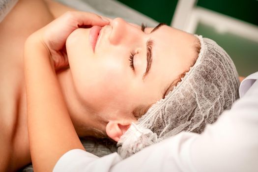 Facial massage. Hands of a masseur massaging neck of a young caucasian woman in a spa salon, the concept of health massage