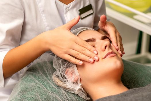 Face massage. Beautiful caucasian young white woman having a facial massage with closed eyes in a spa salon