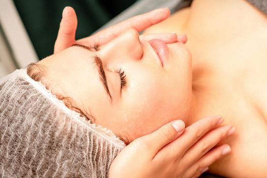 Face massage. Beautiful caucasian young white woman having a facial massage with closed eyes in a spa salon