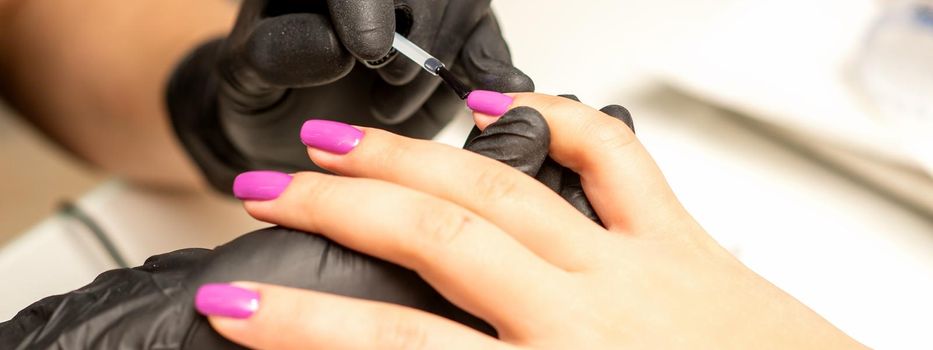 Professional manicure. A manicurist is painting the female nails of a client with purple nail polish in a beauty salon, close up. Beauty industry concept