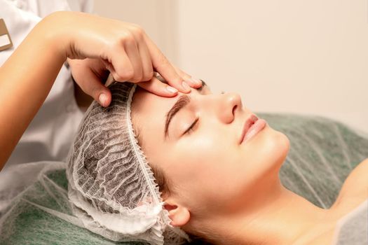 Beautiful caucasian young woman receiving a facial massage with closed eyes in spa salon, close up. Relaxing treatment concept