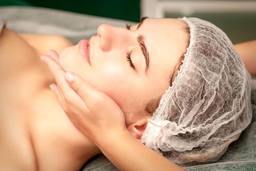 Facial massage. Hands of a masseur massaging neck of a young caucasian woman in a spa salon, the concept of health massage