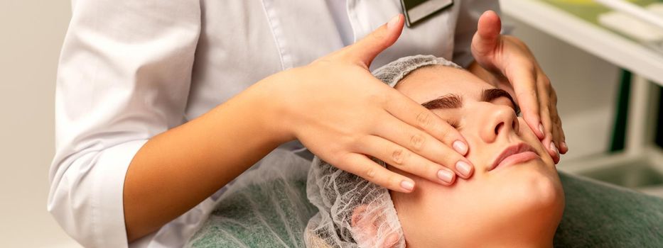 Face massage. Beautiful caucasian young white woman having a facial massage with closed eyes in a spa salon