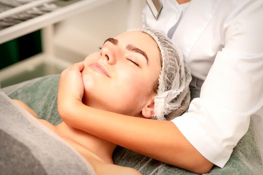 Facial massage. Hands of a masseur massaging neck of a young caucasian woman in a spa salon, the concept of health massage