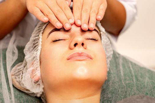 Head massage. Beautiful caucasian young white woman receiving a head and forehead massage with closed eyes in a spa salon