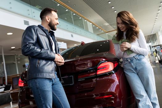 happy young couple choosing a new car in a car dealership with a smile talking to each other.