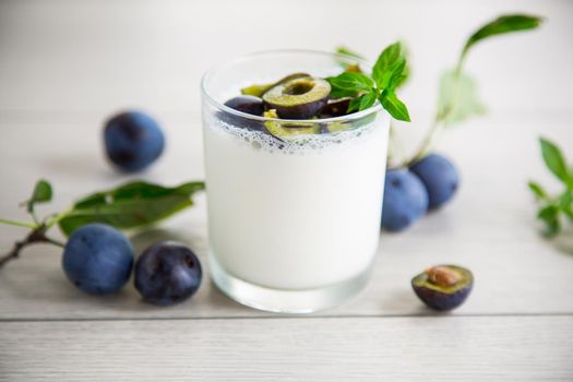 sweet homemade yogurt with fresh plum slices in a glass on a wooden table