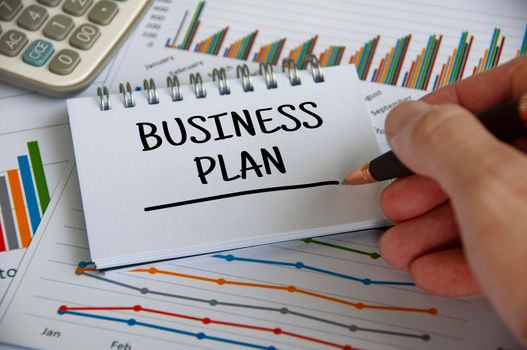 Business plan written on notepad with graph analysis background. Business plan concept.