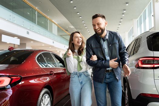 a young couple with smiles on their faces at a car dealership chooses a new car for their family.