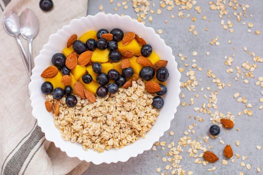 Oatmeal porridge with blueberries, mango and almonds in bowl on concrete grey table from above. flatlay. Healthy breakfast food. Copy space