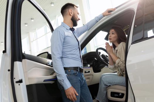 a young woman asks her husband to buy a new car at a car dealership.